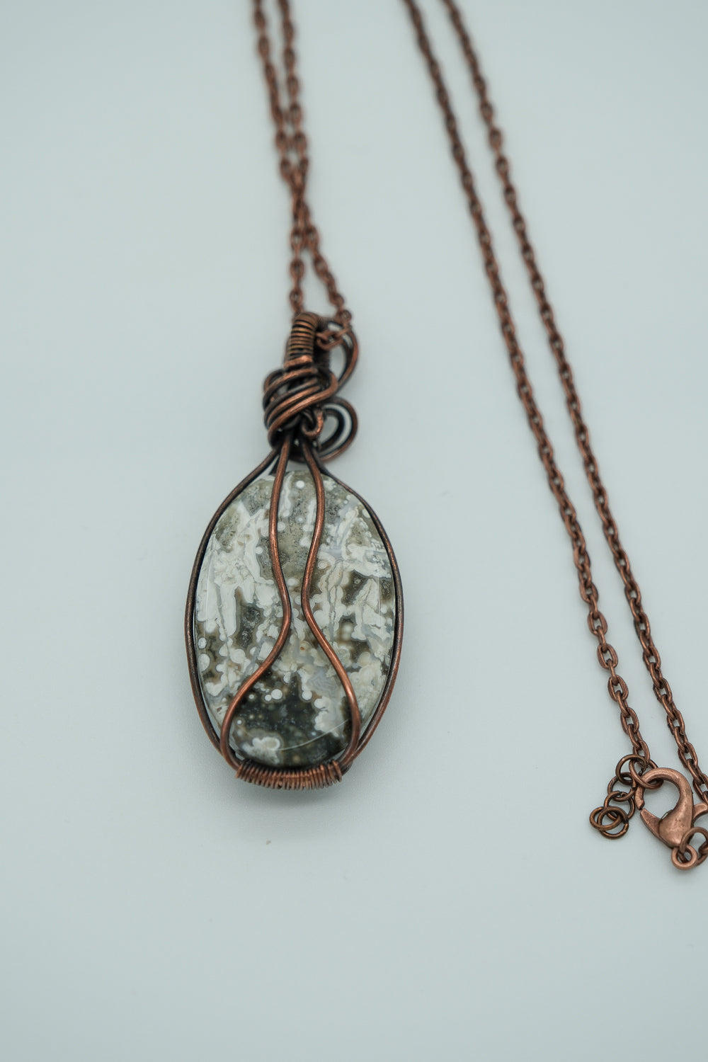 Necklace with a copper wire-wrapped pendant on a light gray background