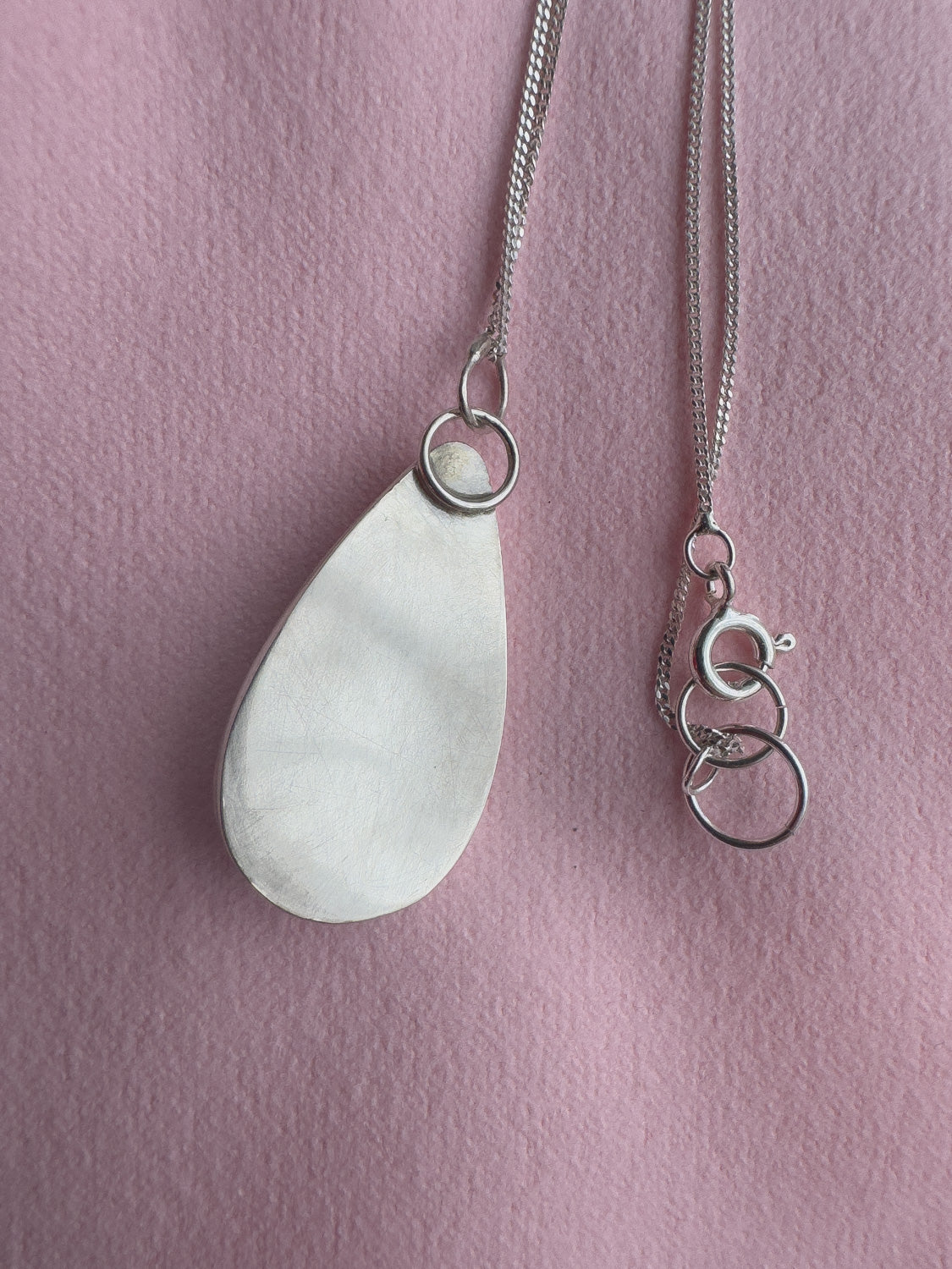 Silver teardrop pendant necklace on a pink background
