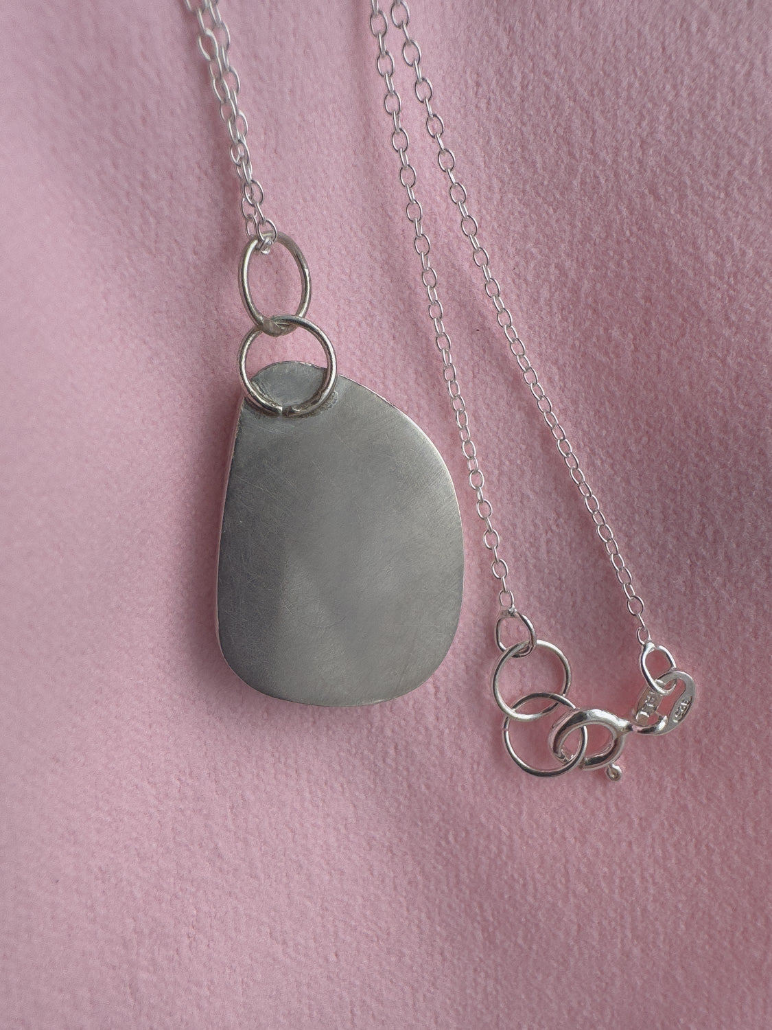 Silver necklace with a teardrop-shaped pendant on a pink background