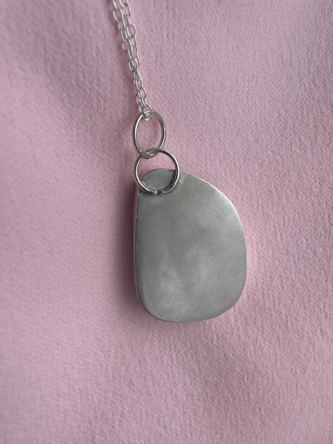 Necklace with a large, teardrop-shaped pendant on a pink background