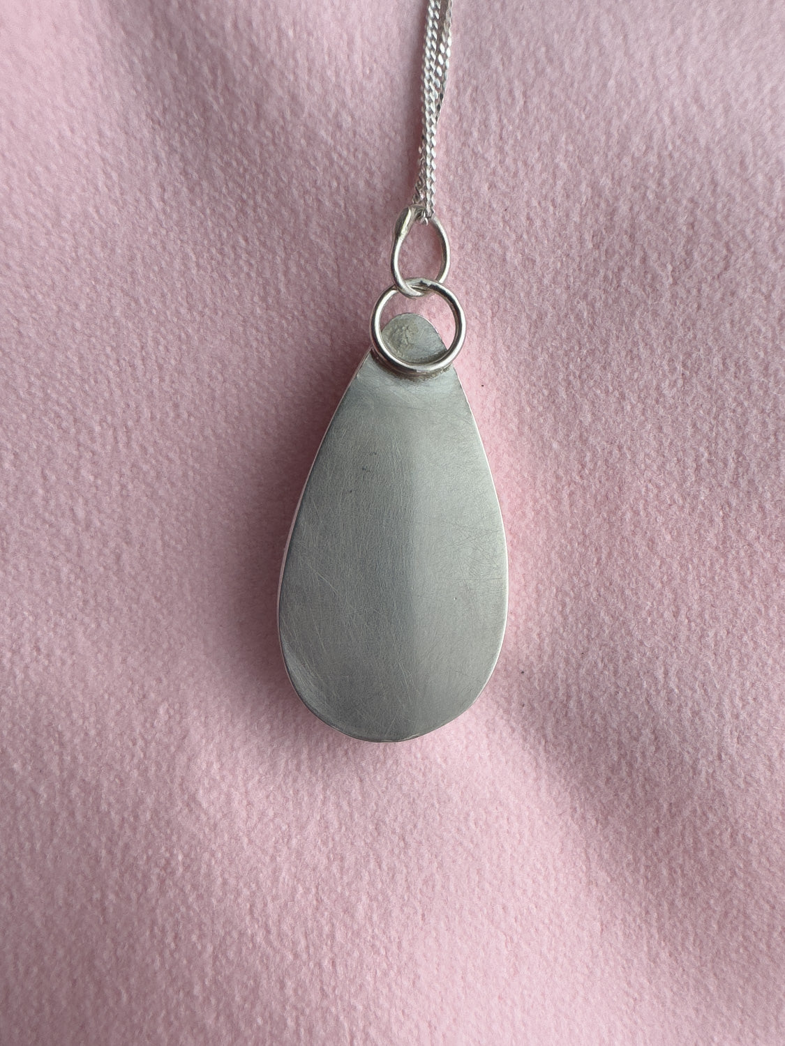 Teardrop-shaped silver pendant on a pink background