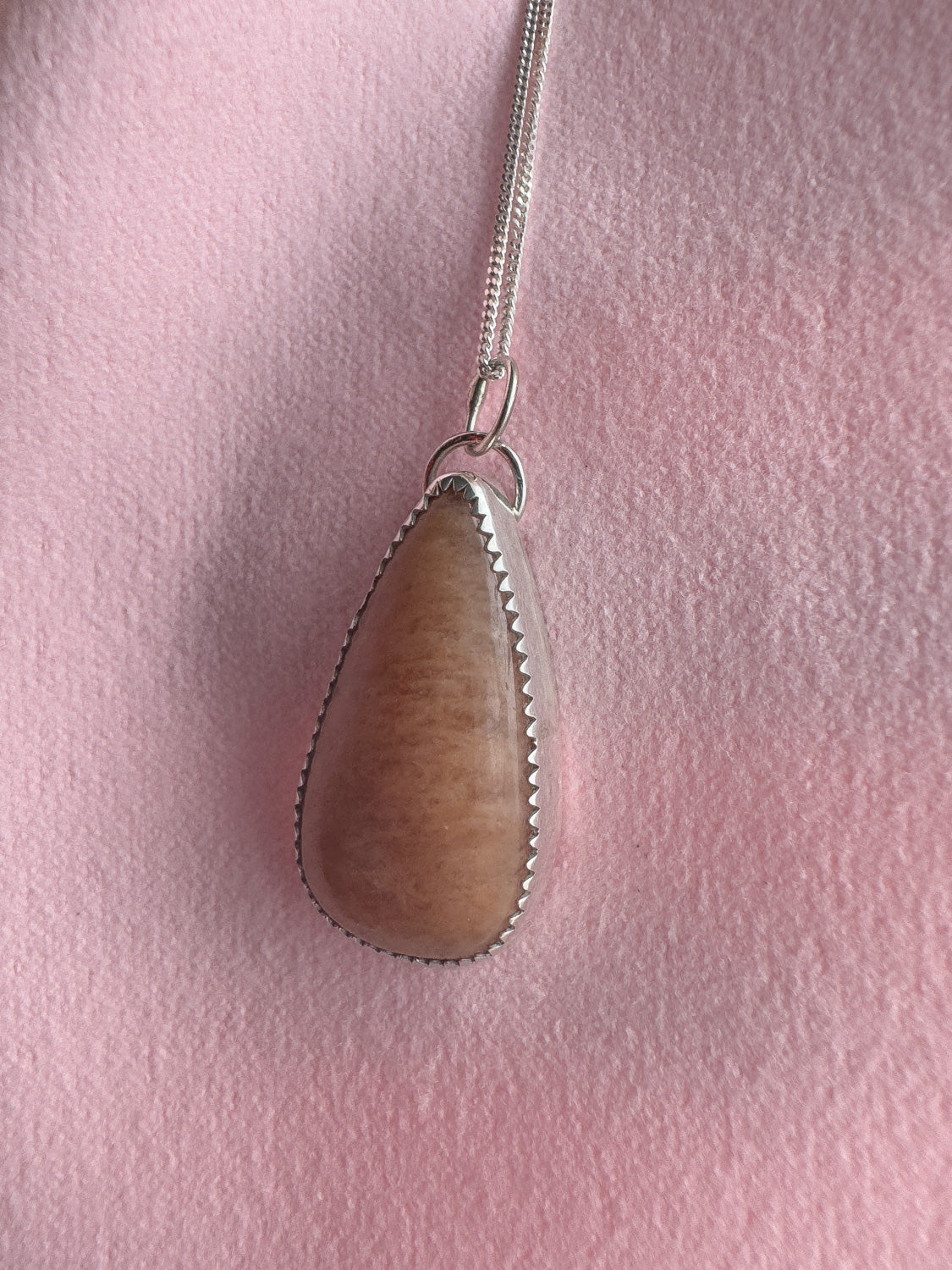 Peach moonstone pendant on a chain against a pink background