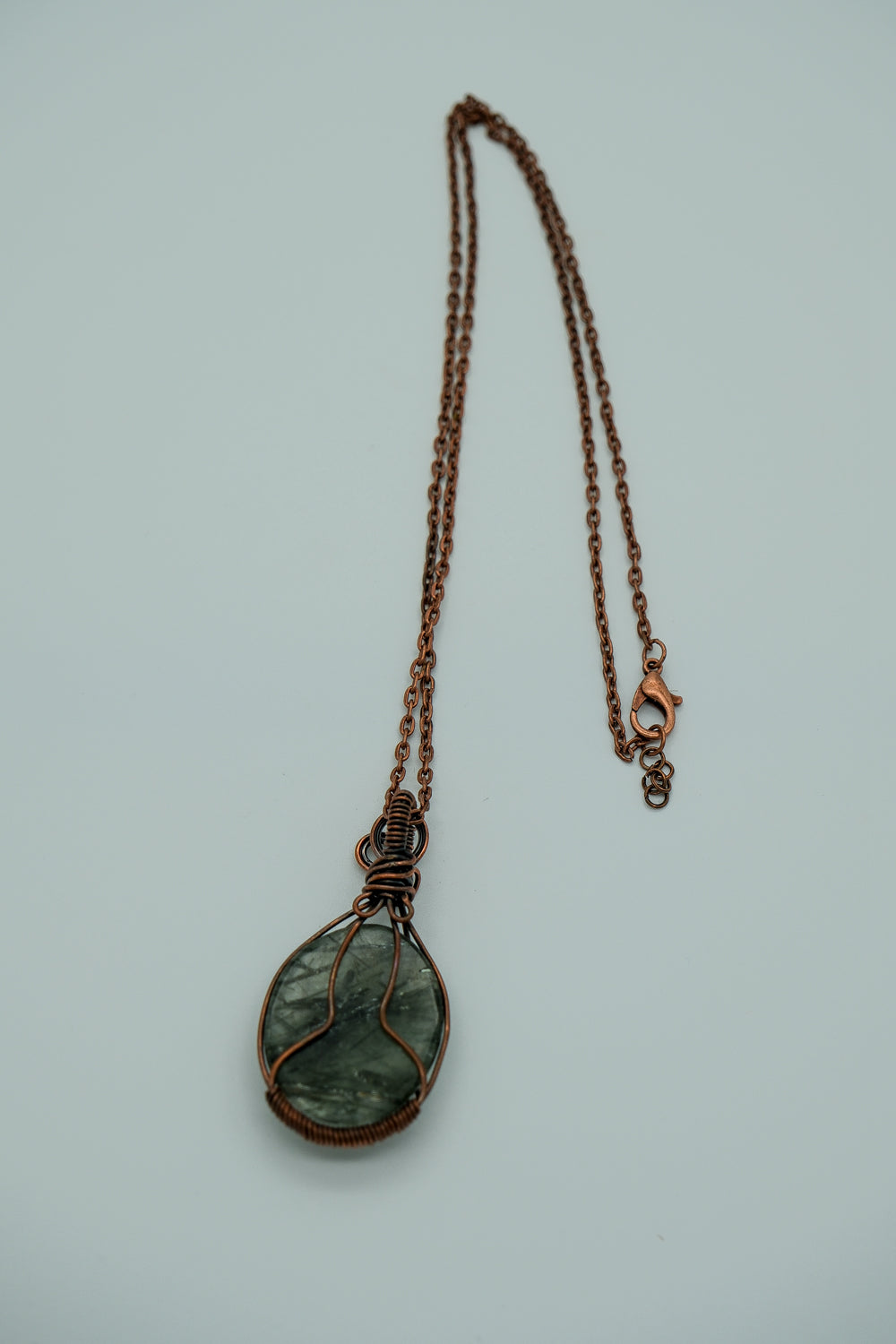 Necklace with a green teardrop pendant on a light gray background