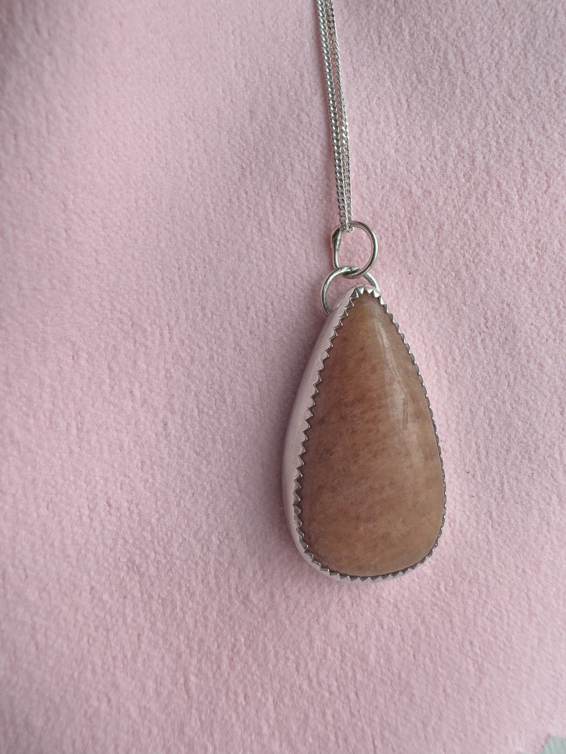 Teardrop-shaped pendant on a chain against a pink background