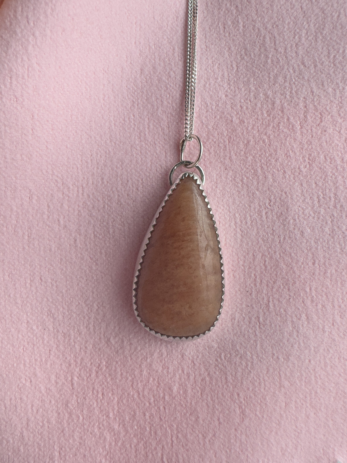 Teardrop-shaped pendant on a chain against a pink background