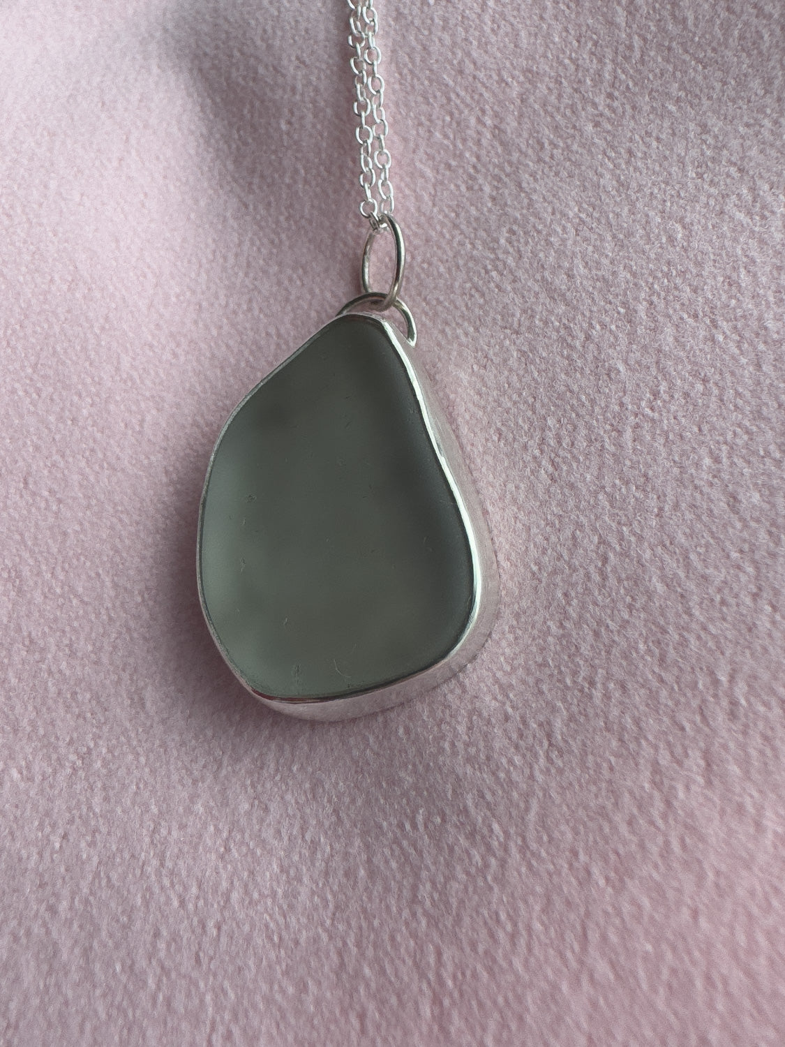 Teardrop-shaped sea glass pendant on a chain against a pink background