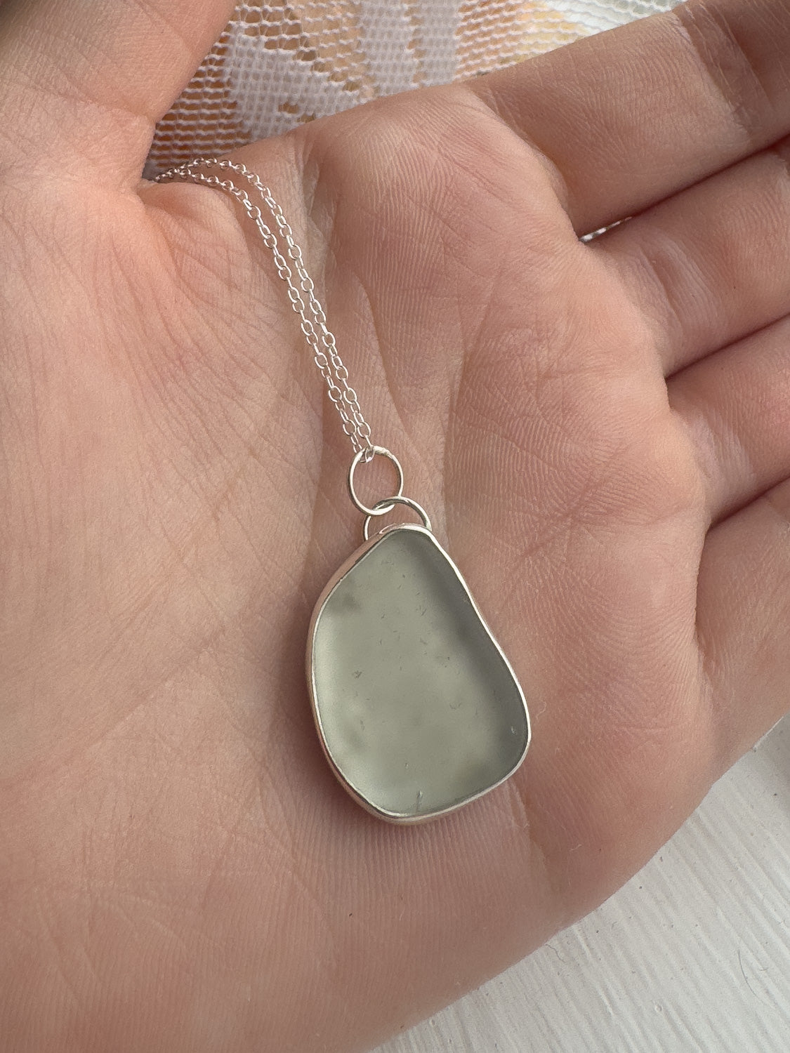 Necklace with a teardrop-shaped pendant held in a hand against a neutral background