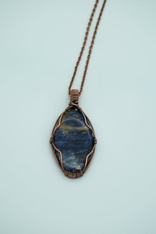 Blue stone pendant with copper wire wrapping on a light blue background