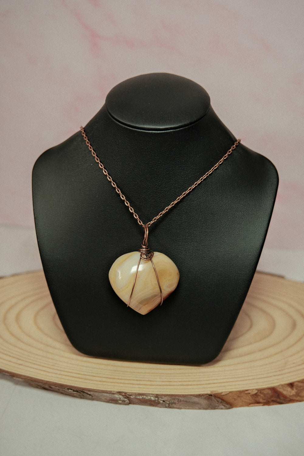 Necklace with a heart-shaped pendant on a black mannequin bust against a light pink background.
