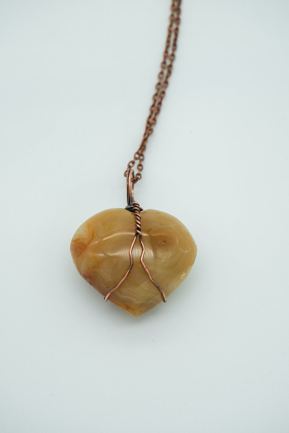 Heart-shaped stone pendant with copper wire wrapping on a chain against a light background