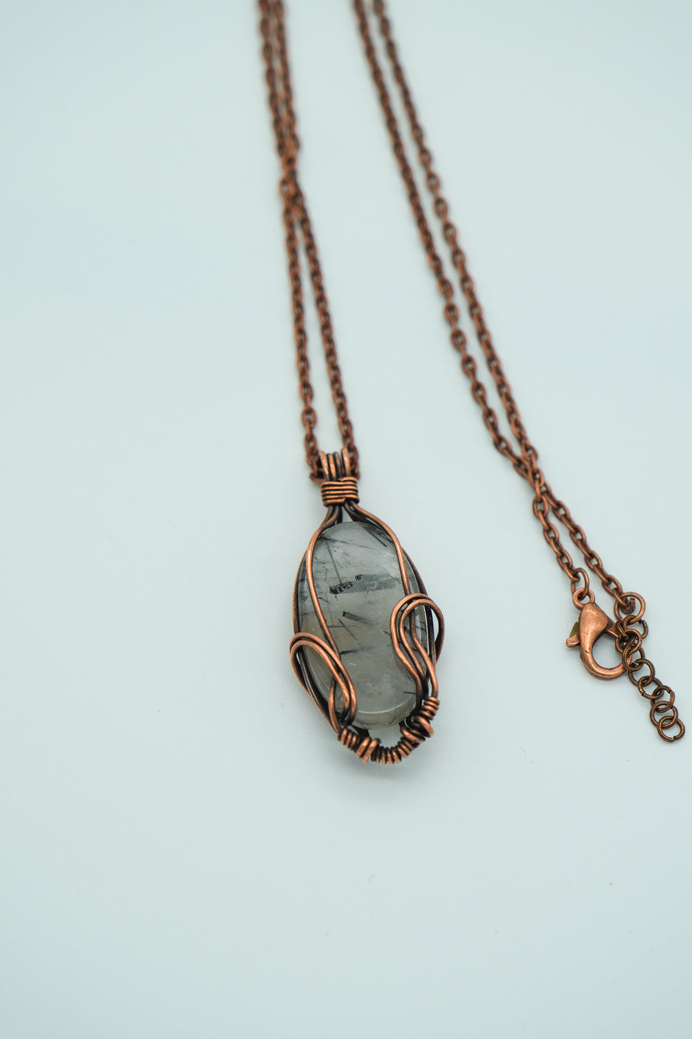 Necklace with a copper-wrapped stone pendant on a light blue background