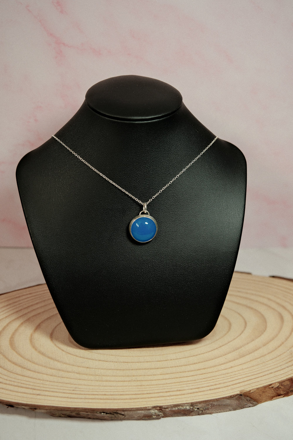 Necklace with a blue pendant on a black bust against a pink background