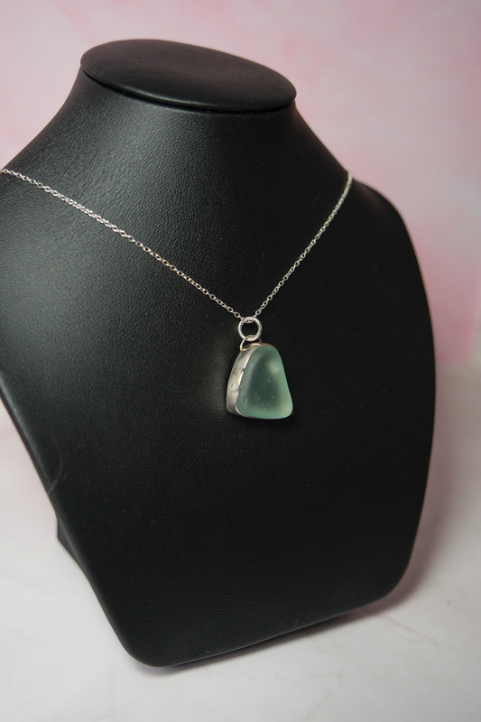 Necklace with a blue pendant on a black mannequin bust against a pink background