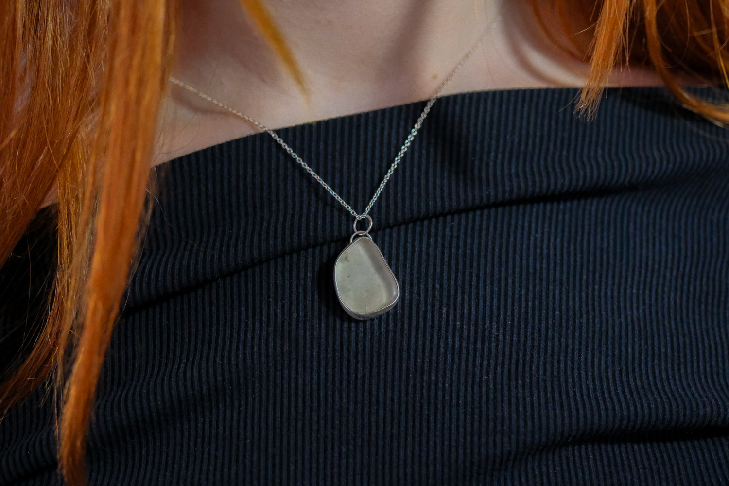 Teardrop-shaped pendant on a necklace worn by a person with red hair.