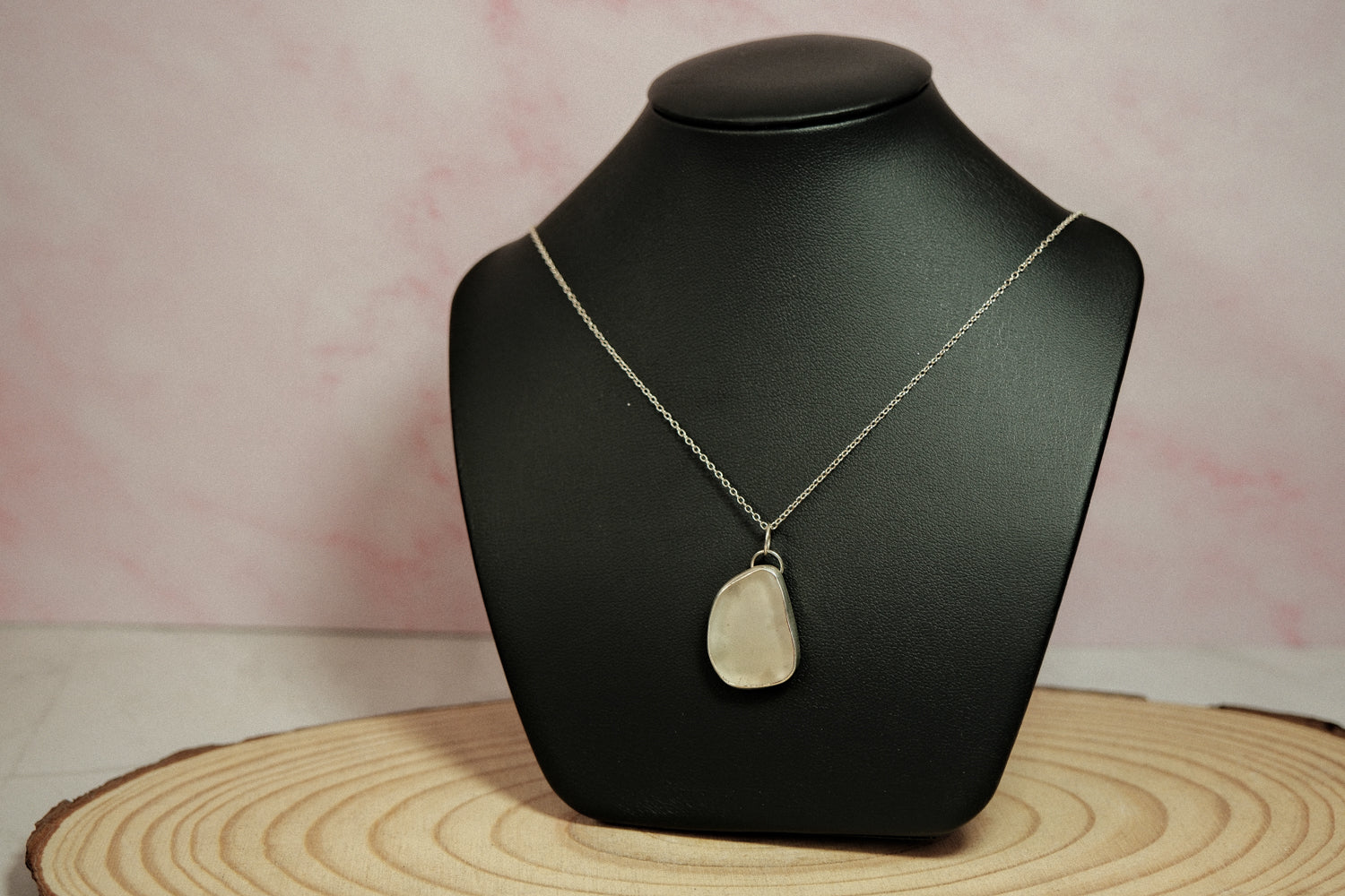 Necklace with a pendant on a black mannequin bust against a pink background