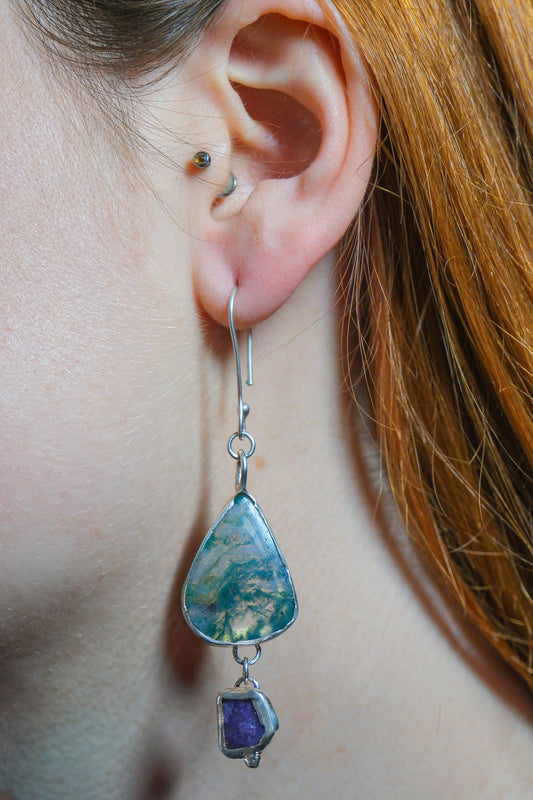 Close-up of an ear wearing a teardrop-shaped earring with a purple gemstone.
