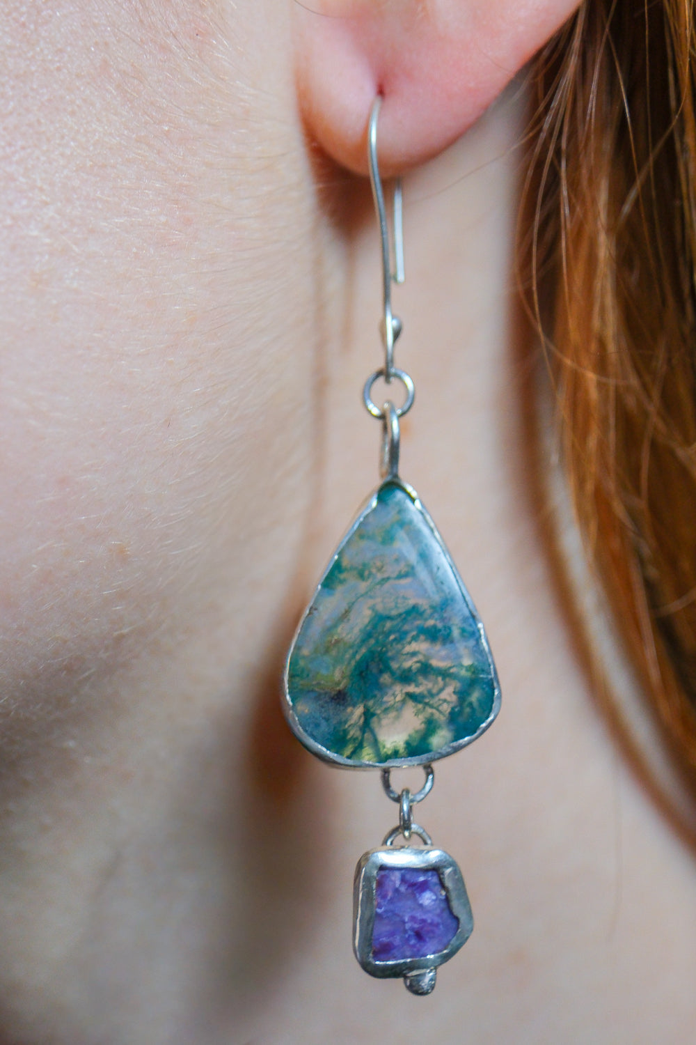 Teardrop-shaped earrings with a purple gemstone worn by a person.