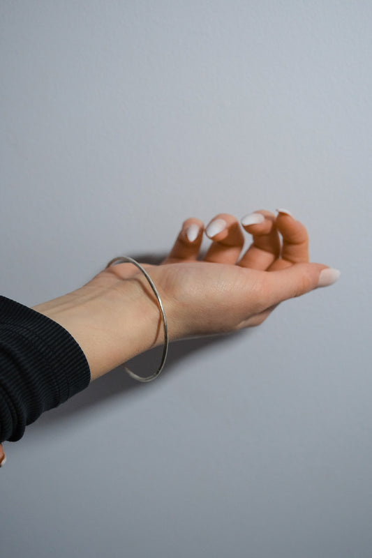 Hand wearing a silver bracelet on a plain background