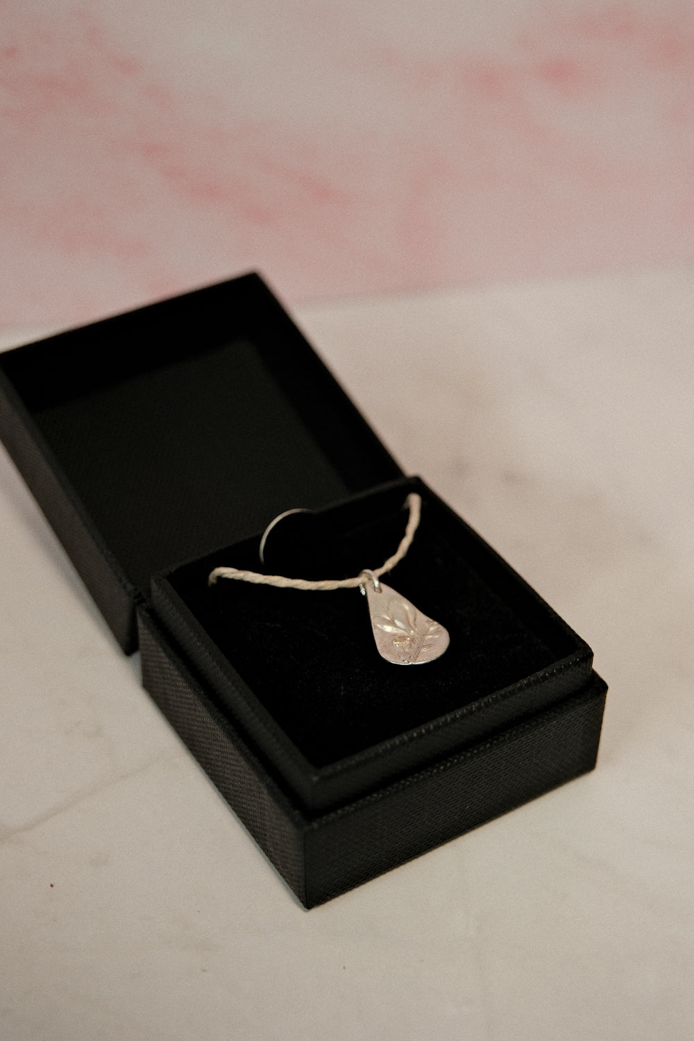 Silver necklace with a pendant in an open black jewelry box on a light pink background