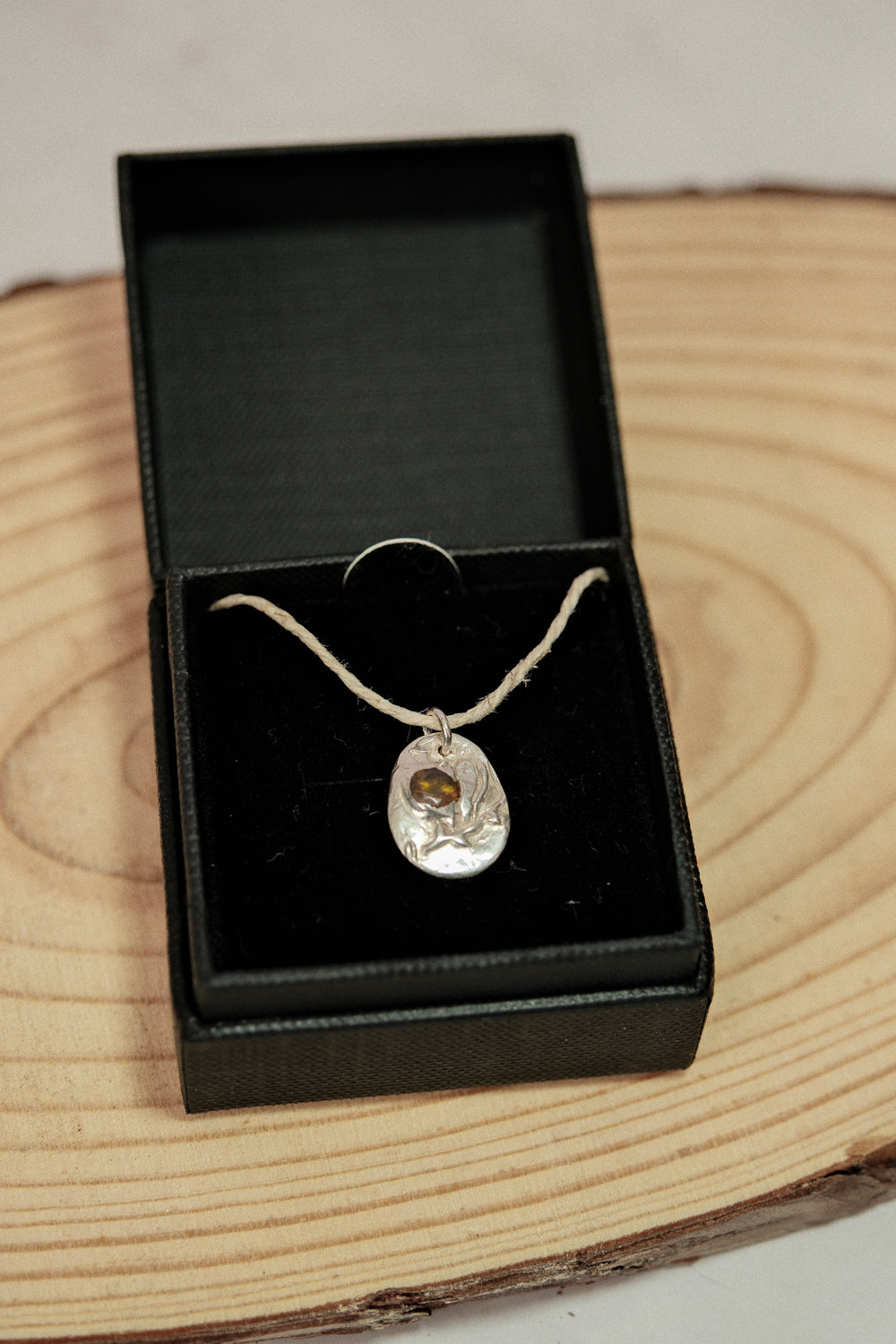 Silver necklace with a pendant in a black jewelry box on a wooden surface