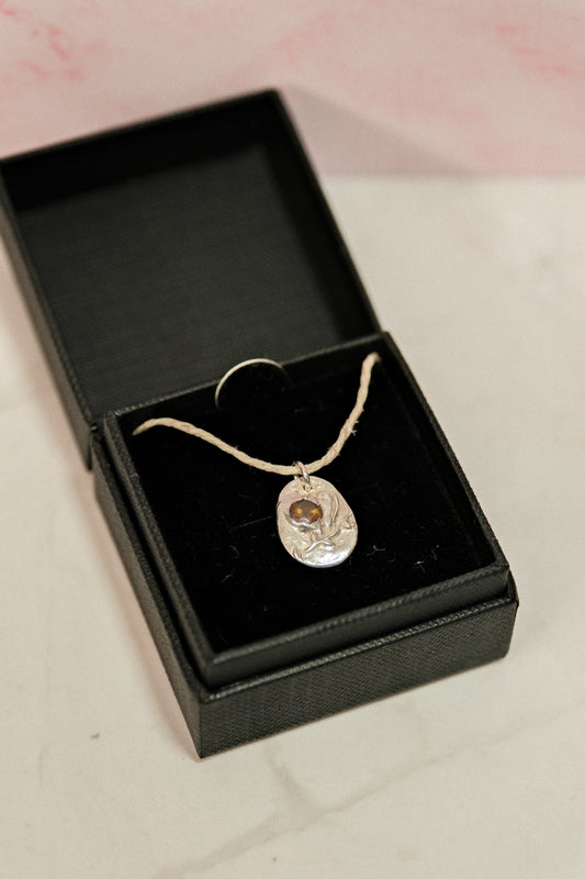 Silver necklace with a pendant in an open black jewelry box on a light pink background