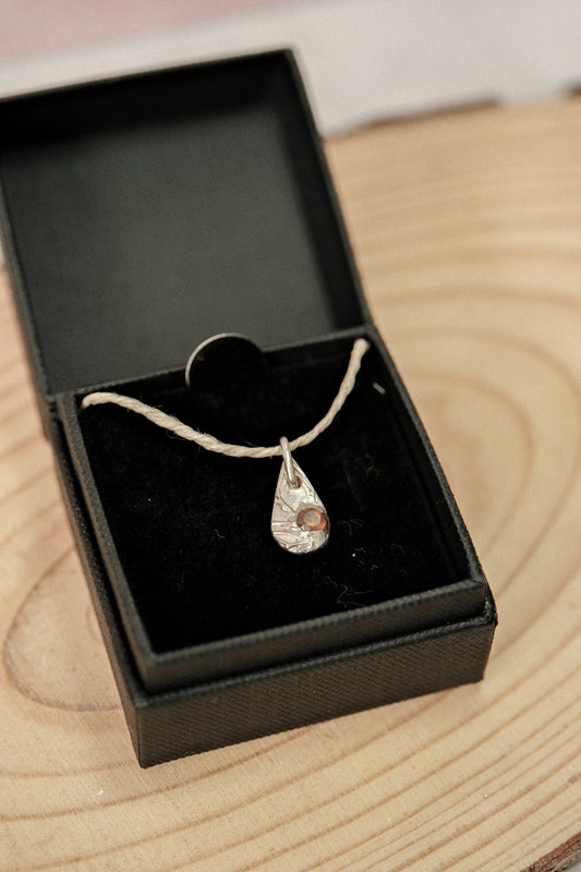 Necklace with a teardrop pendant in an open black jewelry box on a wooden surface