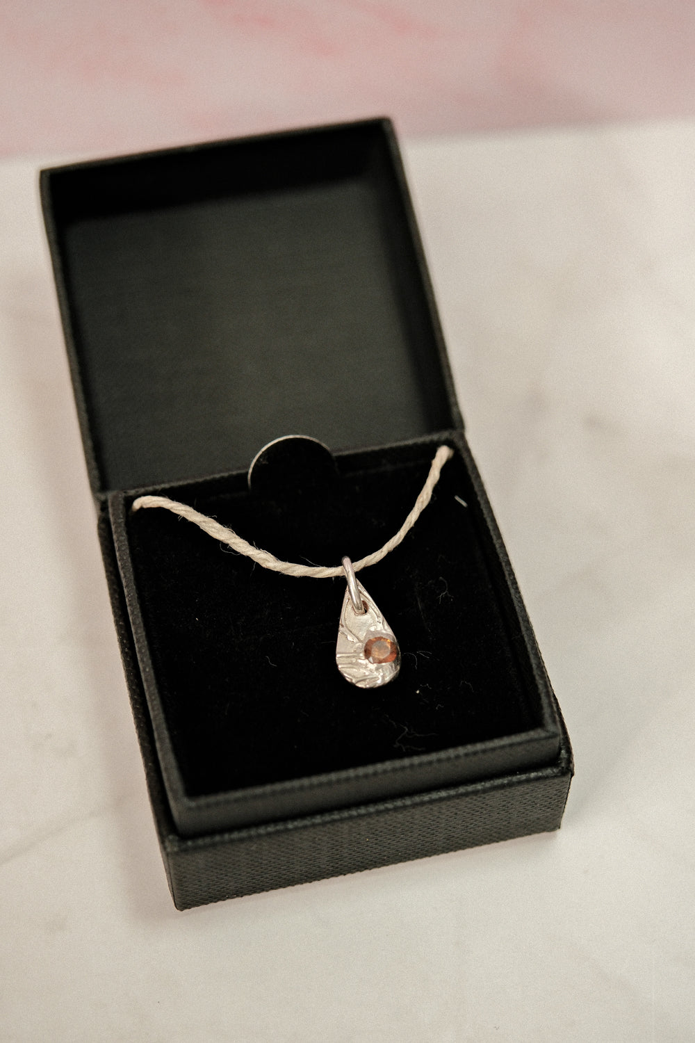 Necklace with a teardrop-shaped pendant in a black jewelry box on a light pink background