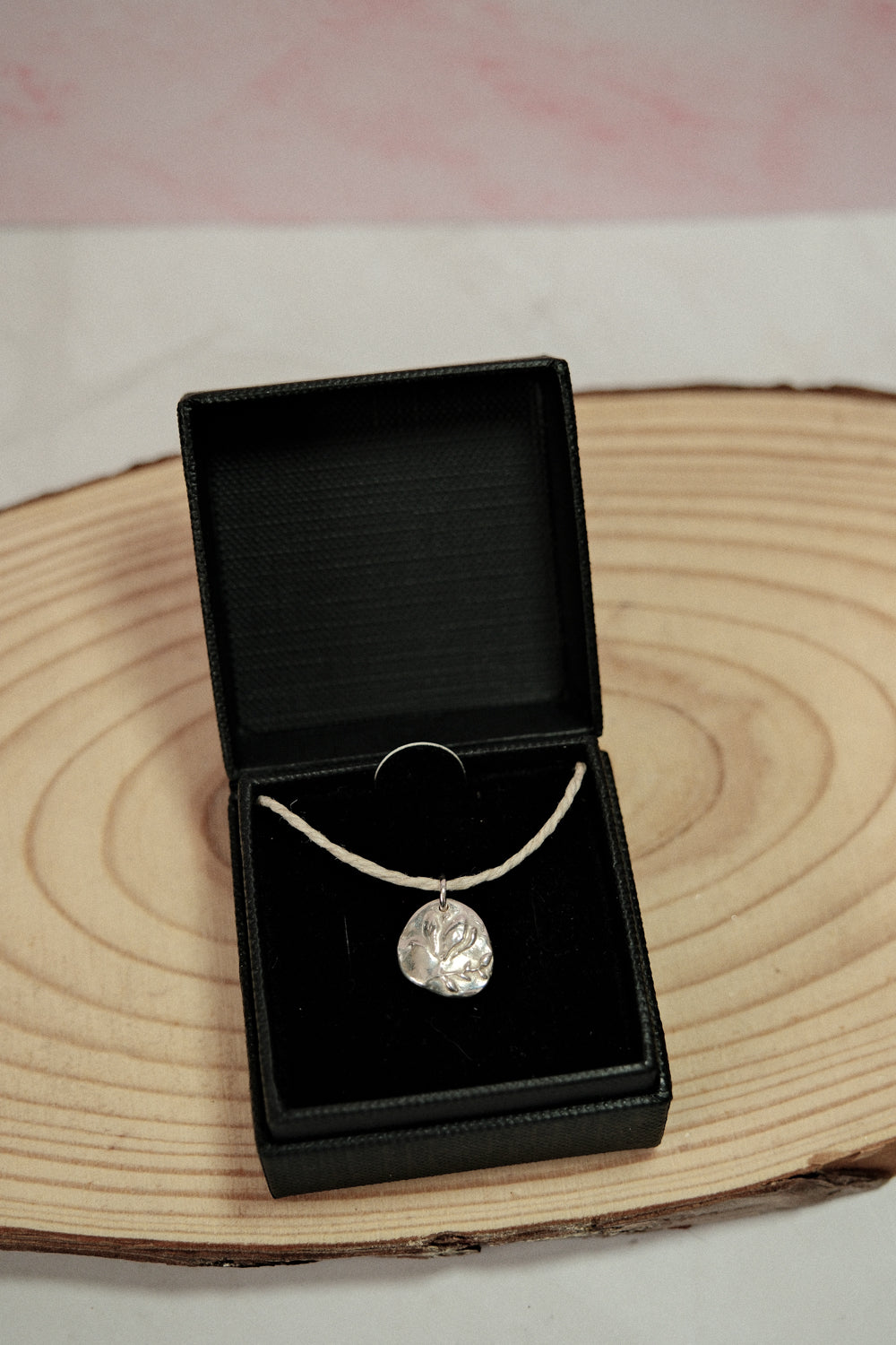 Silver necklace with a pendant in an open black jewelry box on a wooden surface.