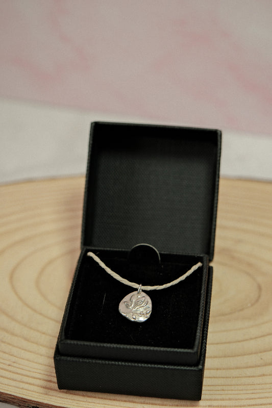 Silver necklace with a pendant in an open black jewelry box on a wooden surface.