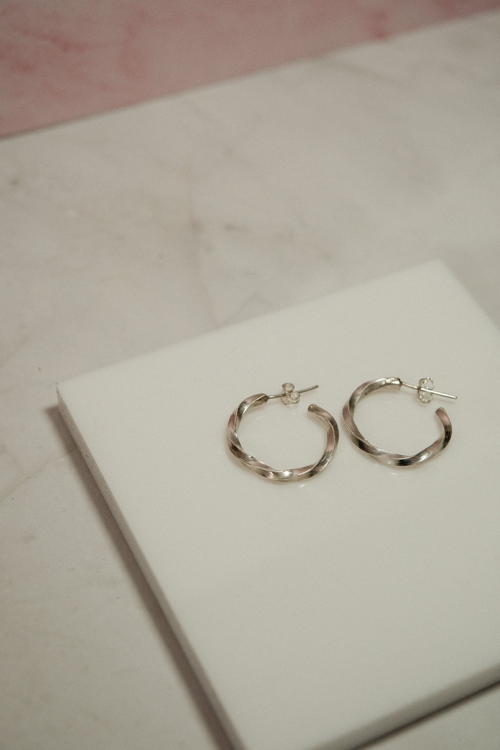 Silver hoop earrings on a white box with a pink background