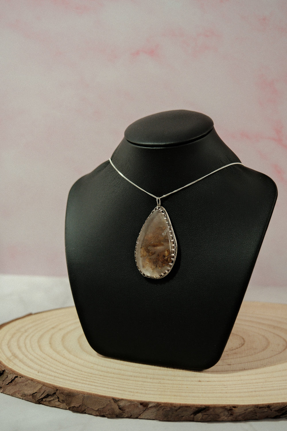 Necklace with a large pendant on a black mannequin bust against a pink background