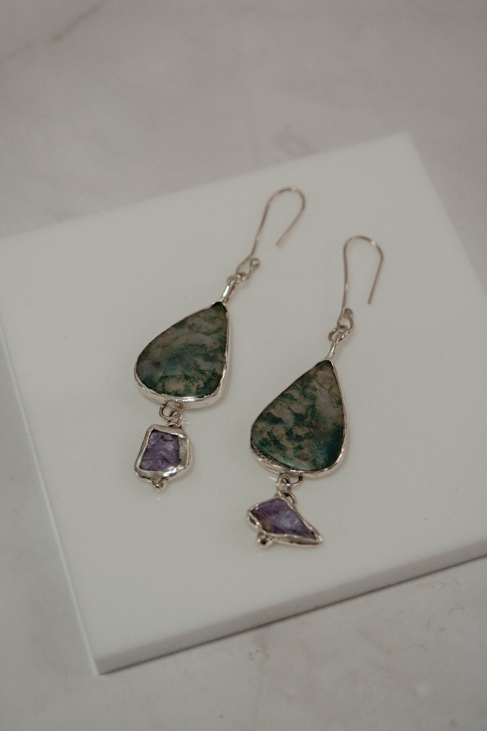 Pair of earrings with green and purple stones on a white surface