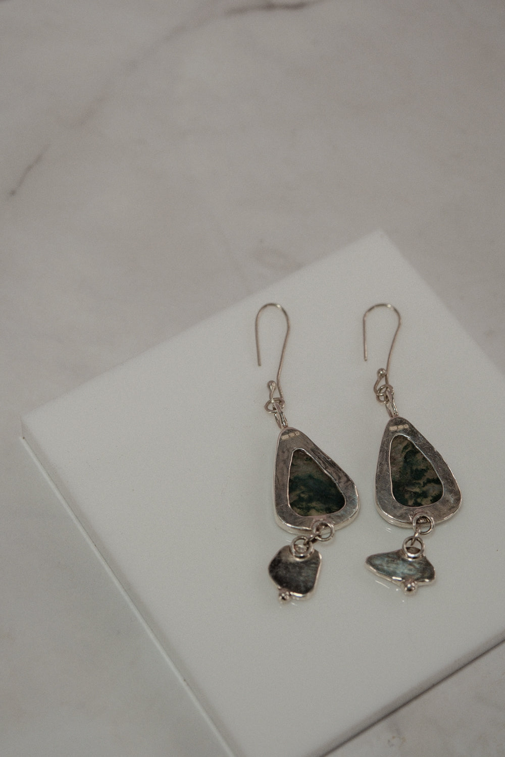 Pair of silver earrings with green stones on a white surface