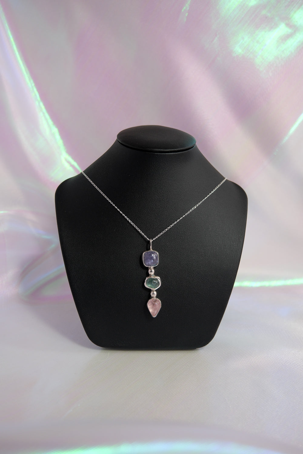 Necklace with a pendant on a black mannequin bust against a soft pink background