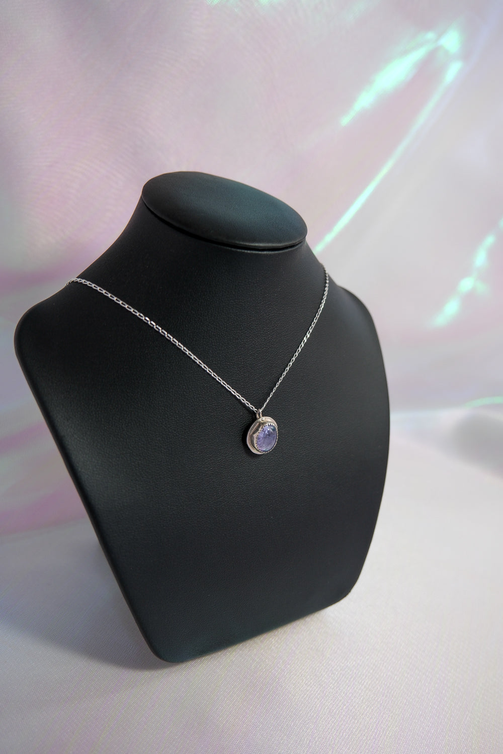 Necklace with a purple pendant on a black mannequin bust against a light pink background