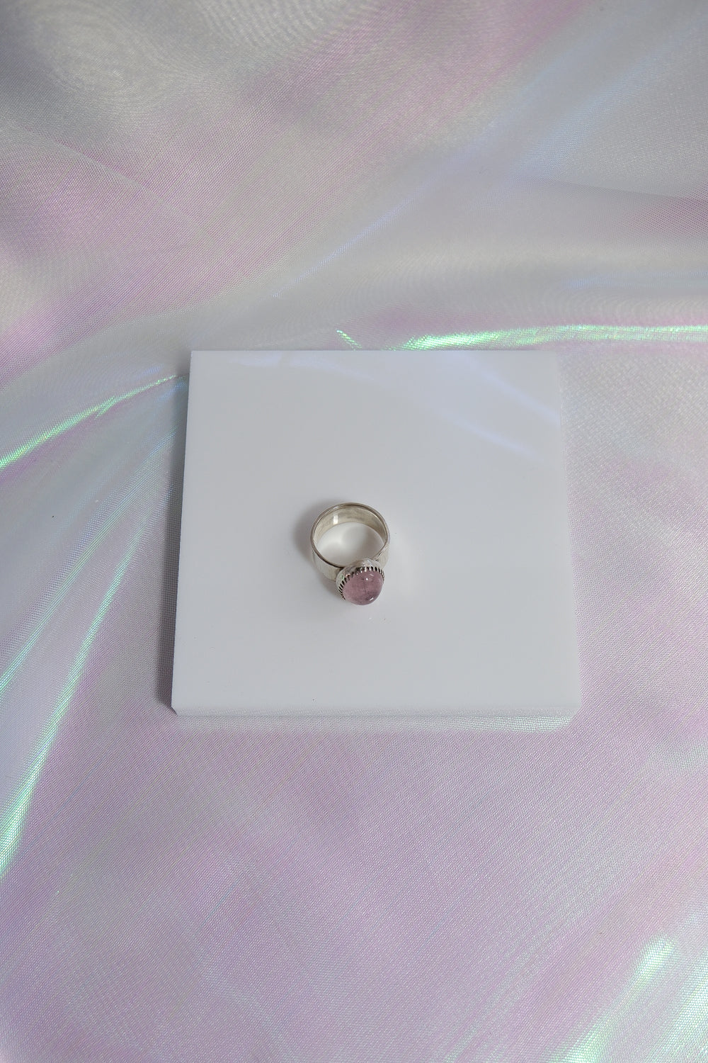 Silver ring with a pink stone on a white card against a reflective surface