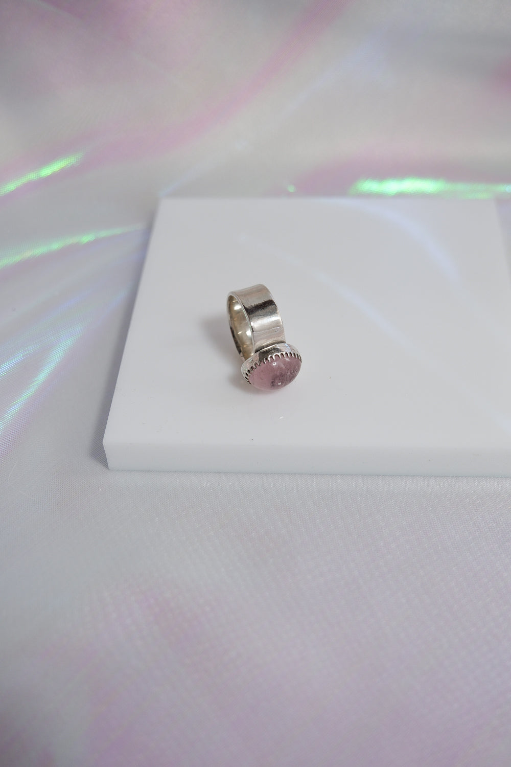 Silver ring with a pink gemstone on a white box with a colorful background