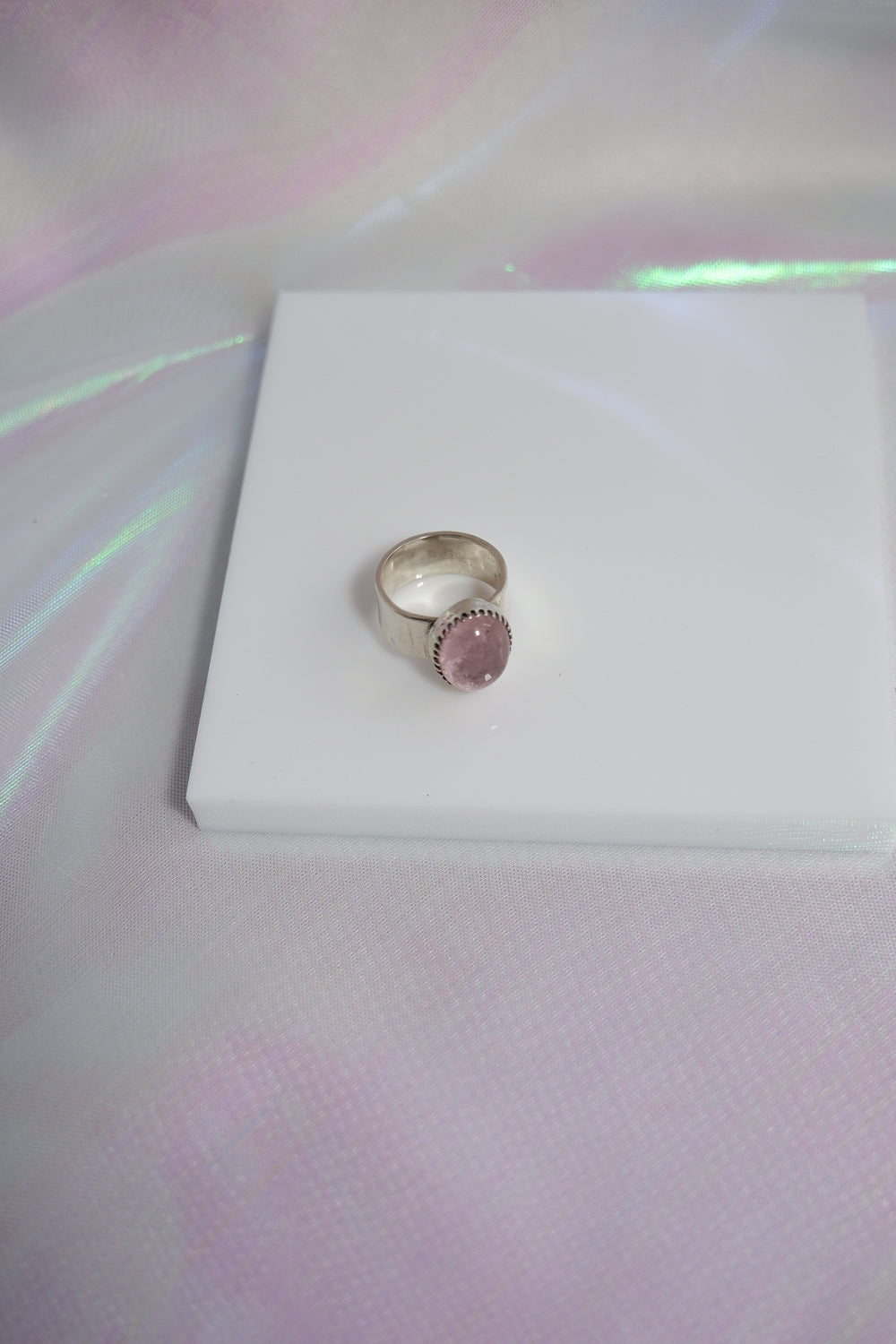 Silver ring with a pink gemstone on a white box with a pink and white gradient background