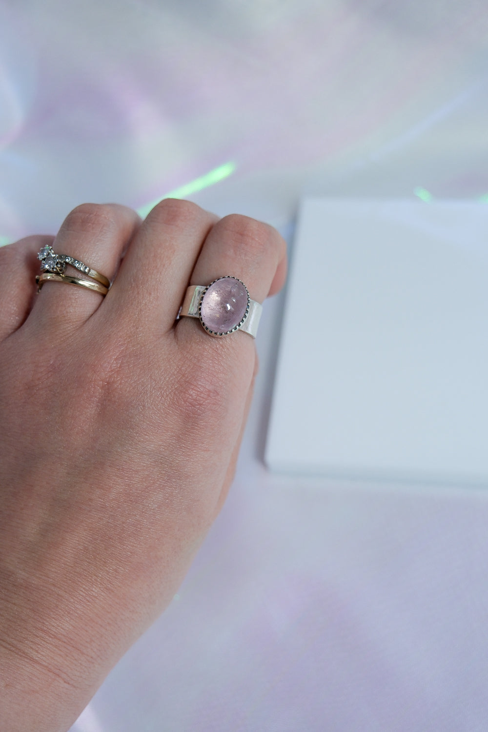 Hand wearing a ring with a pink stone on a light background