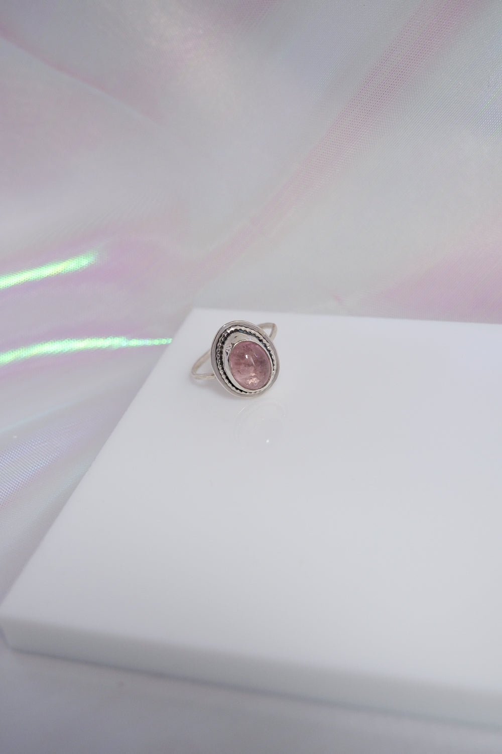 Silver ring with a pink gemstone on a white surface with a colorful background