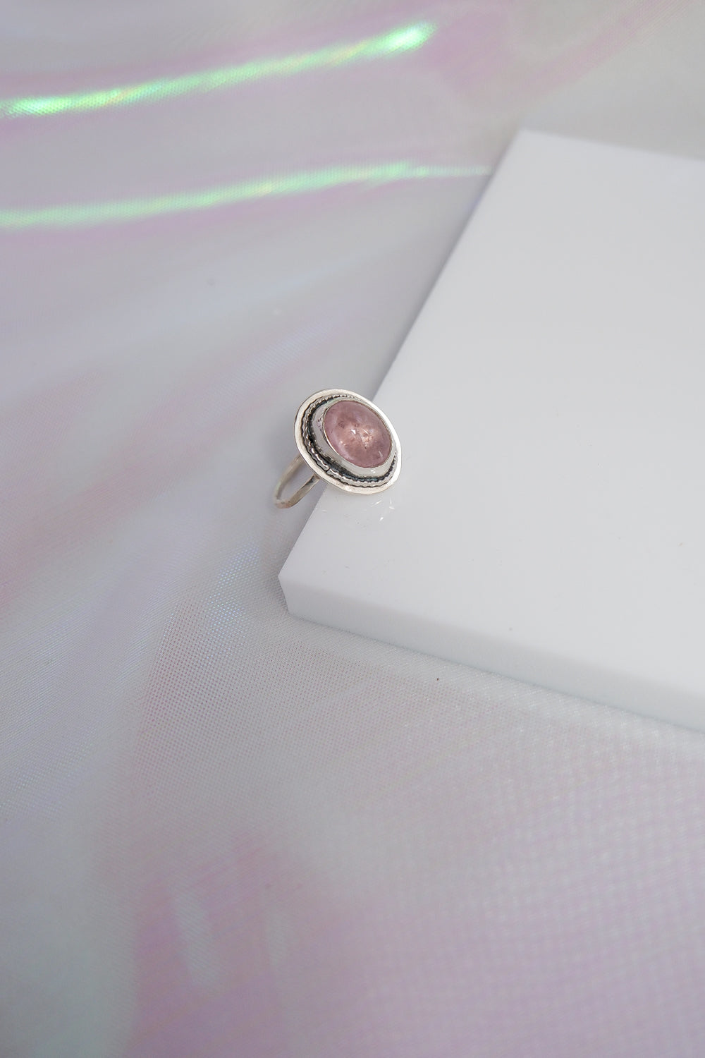 Silver ring with a pink stone on a white surface