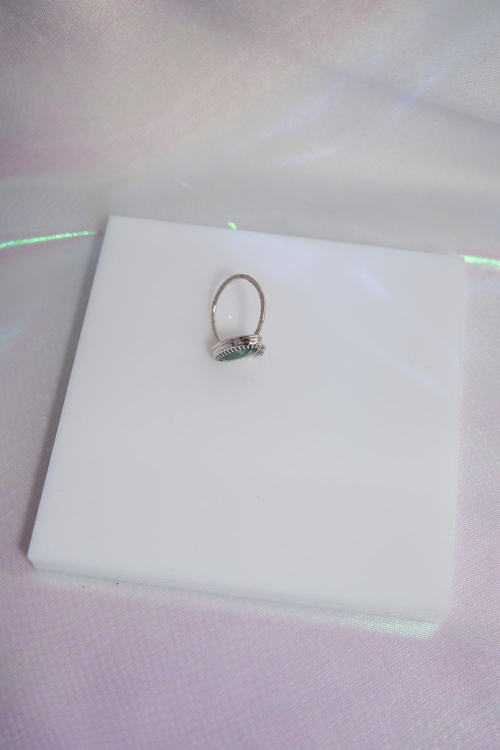 Silver ring on a white square pad with a light purple background
