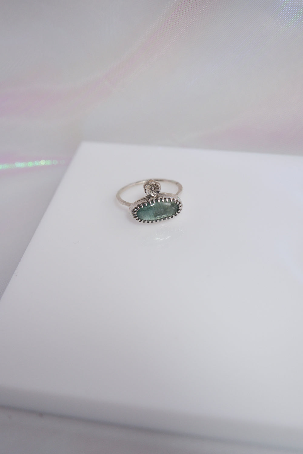 Silver ring with a green gemstone on a white surface