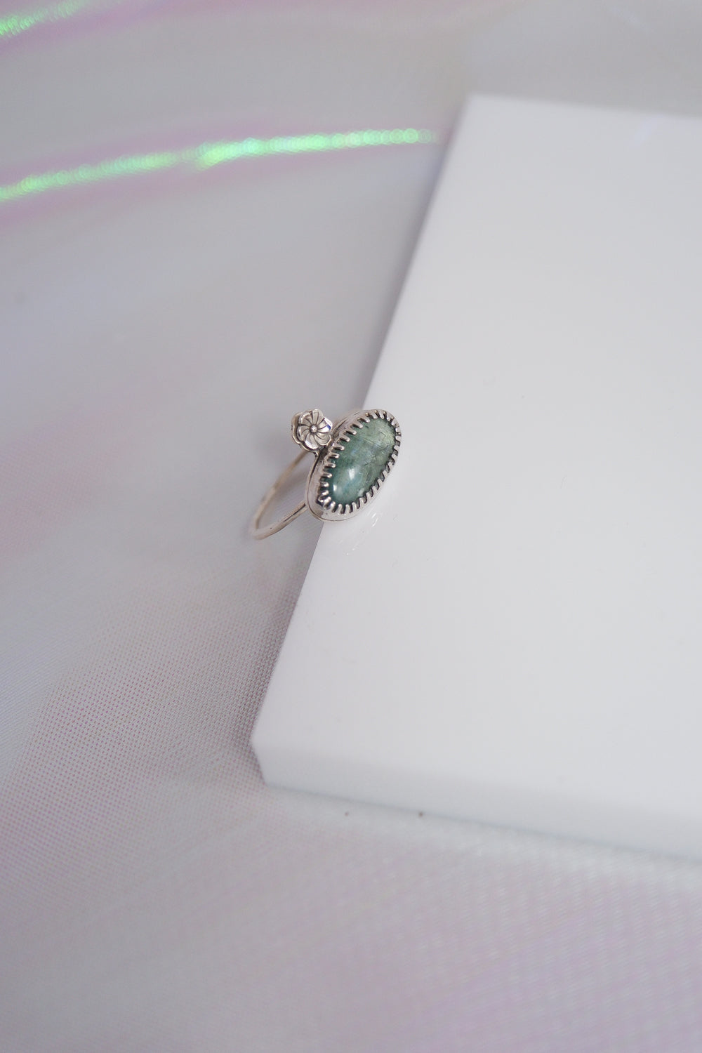 Silver ring with a green gemstone on a white cushion