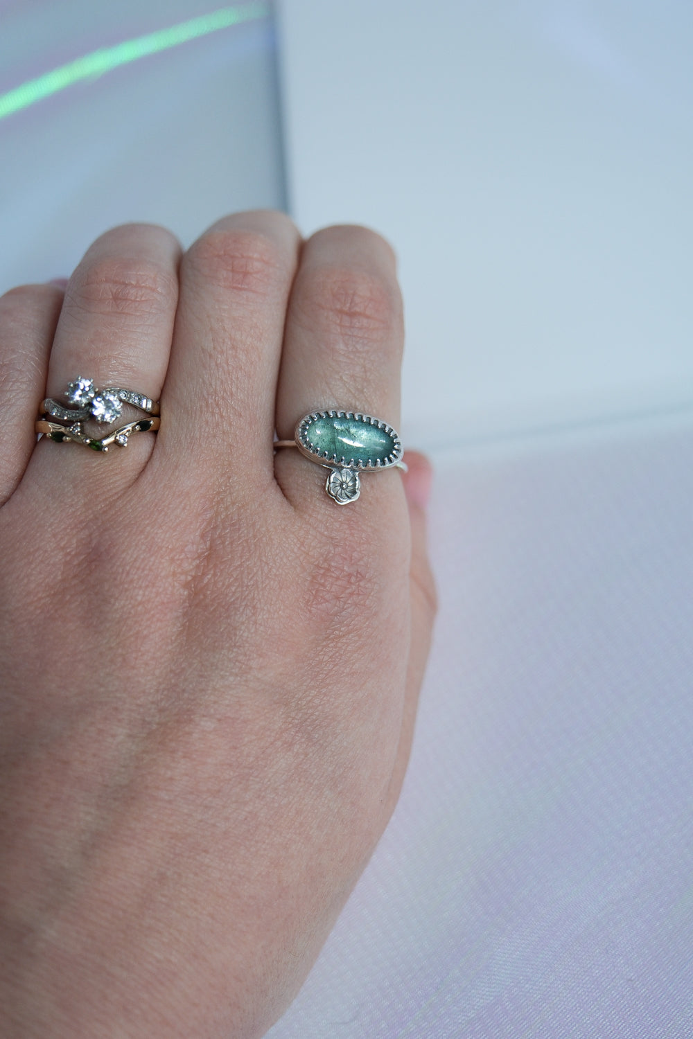 Hand wearing two rings with a green gemstone on a white background