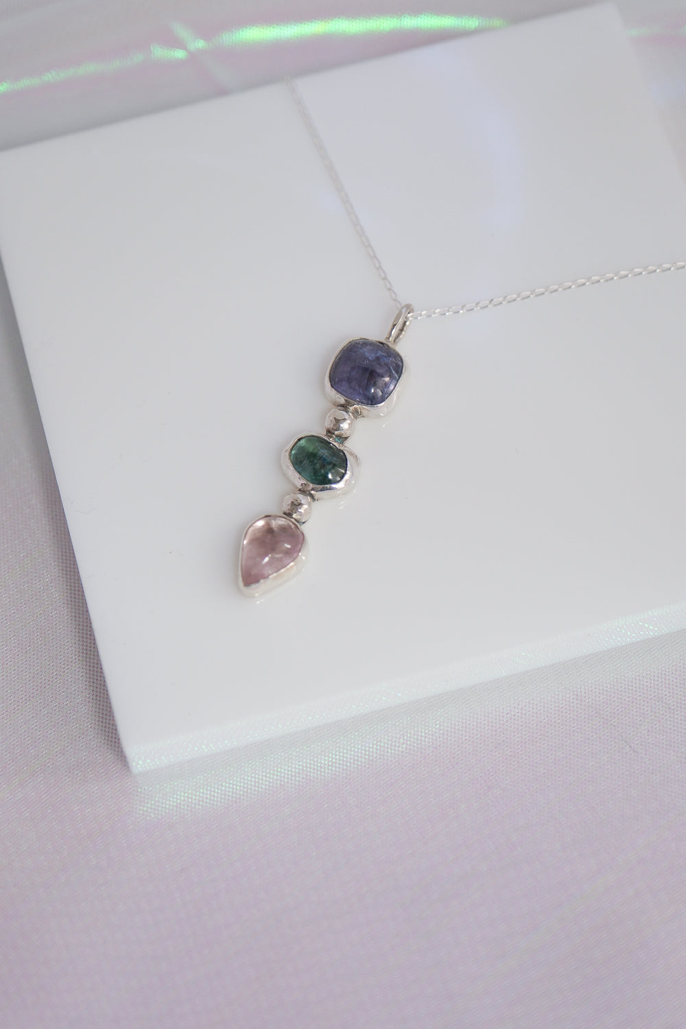 Silver necklace with three colored gemstones on a white background