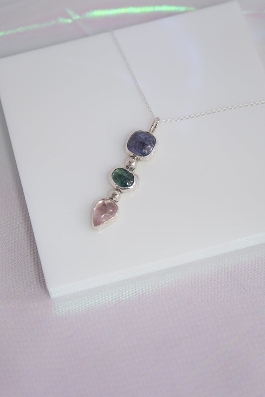 Silver necklace with three colored gemstones on a white background