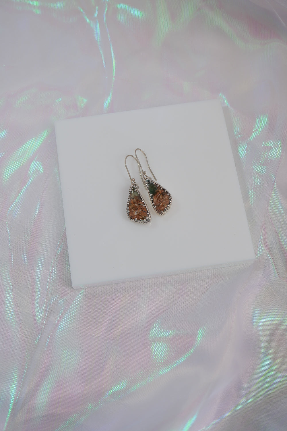 Pair of earrings on a white box with a colorful, patterned background