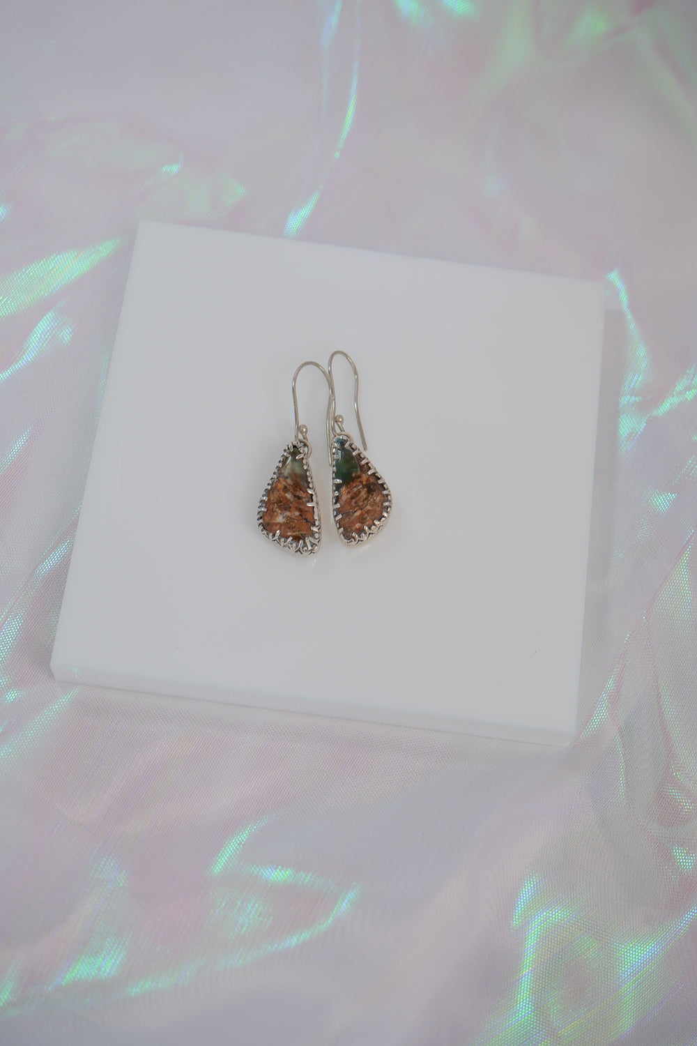 Teardrop-shaped earrings on a white box with a colorful, blurred background