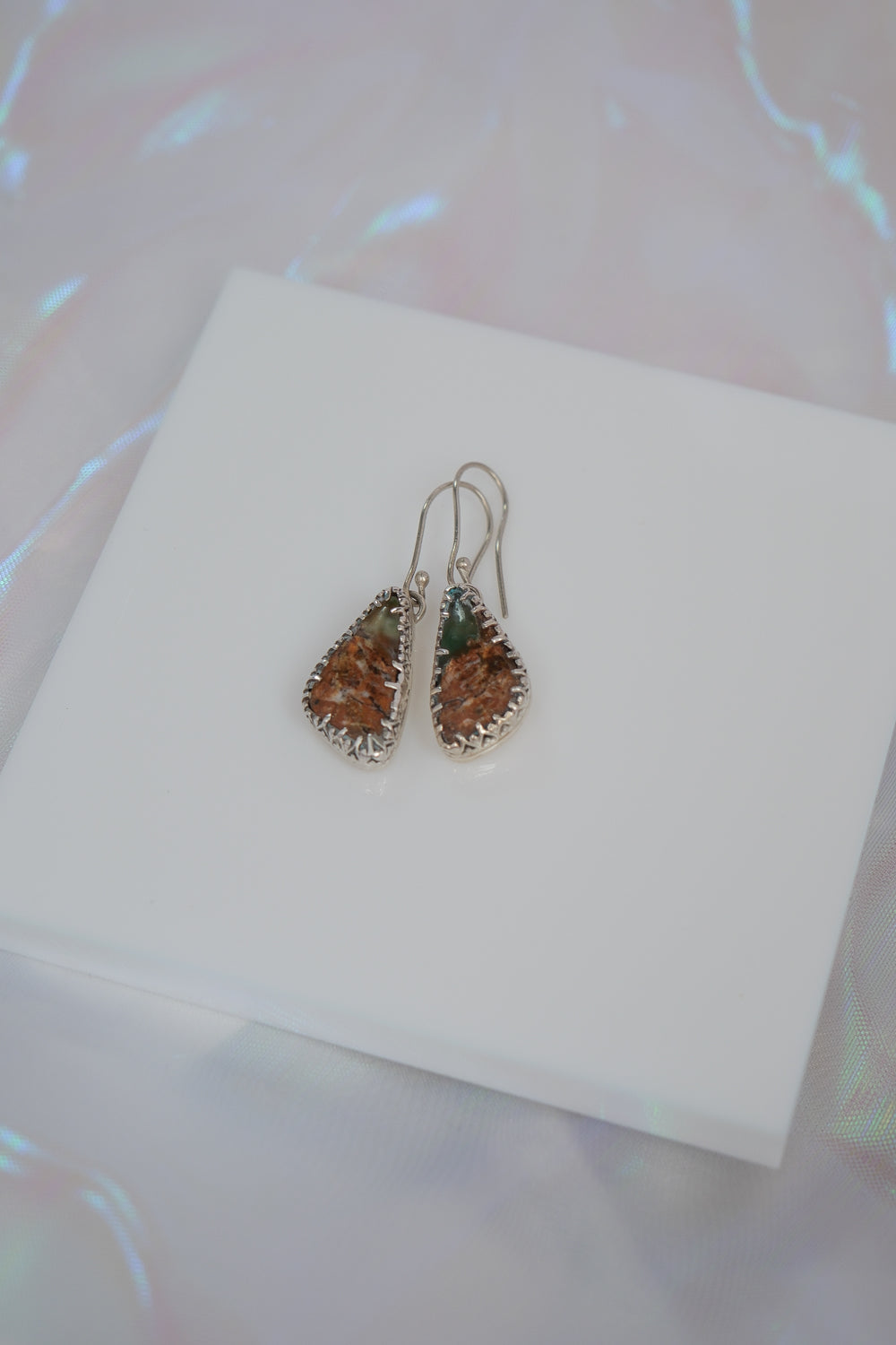 Teardrop-shaped earrings on a white card with a blurred background